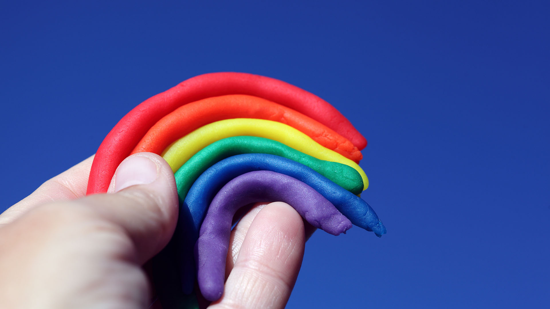 A hand holding a colorful rainbow made with clay.