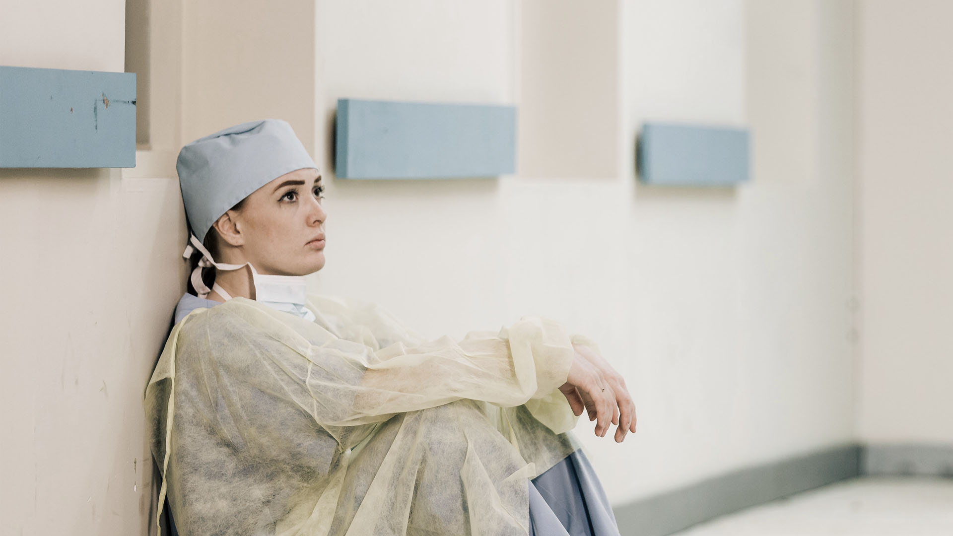A doctor sitting against a wall, wearing surgical gown and ppe.