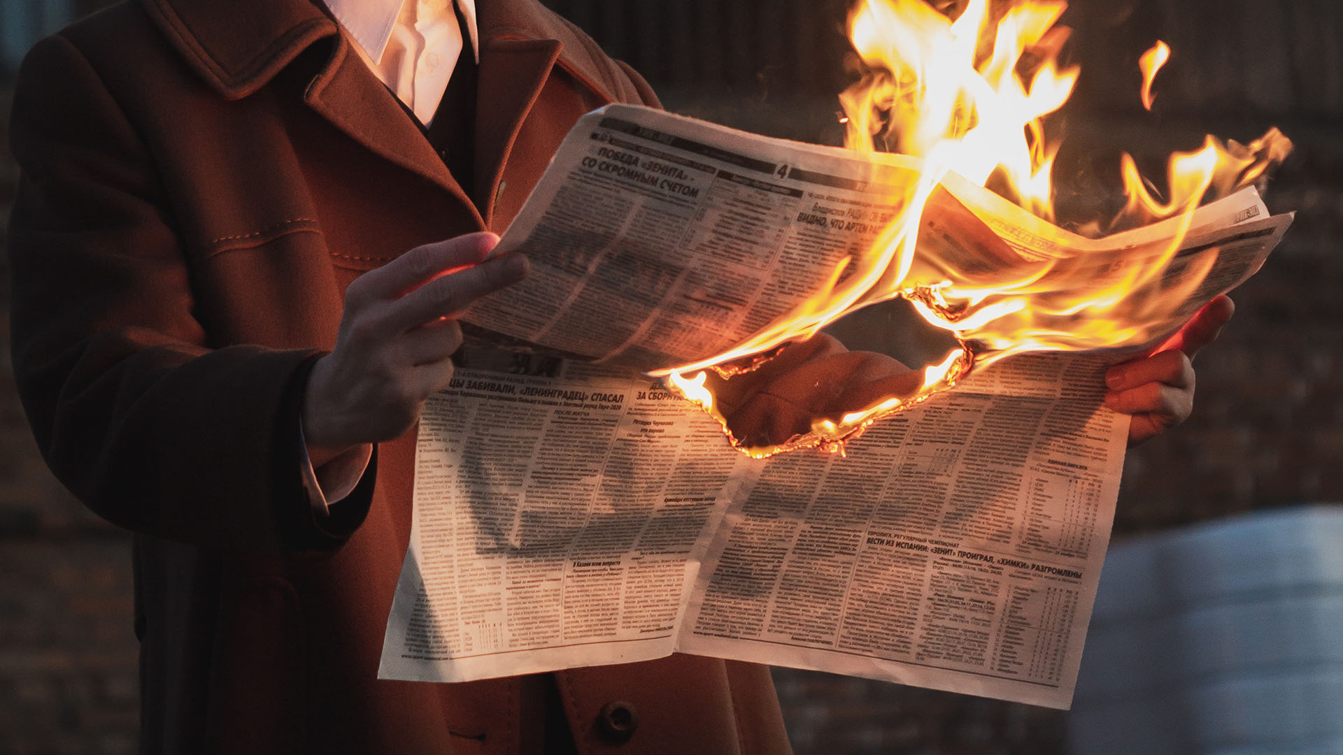 A man holding a burning news paper.