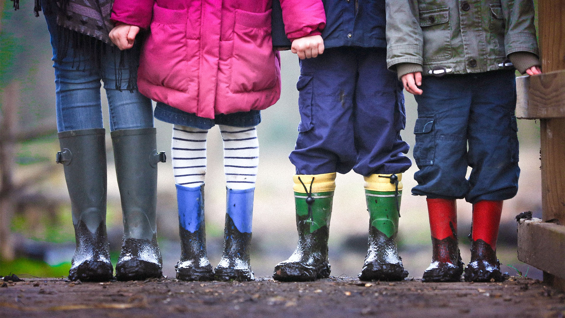 Close up of four kids standing outside in their rain boots.