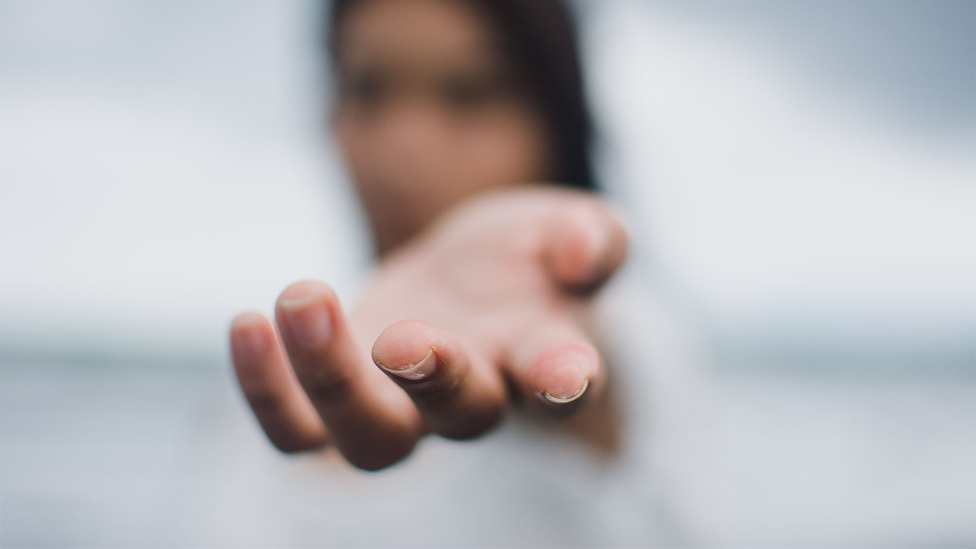 A woman's hand reaching out with her blurry face in the background.