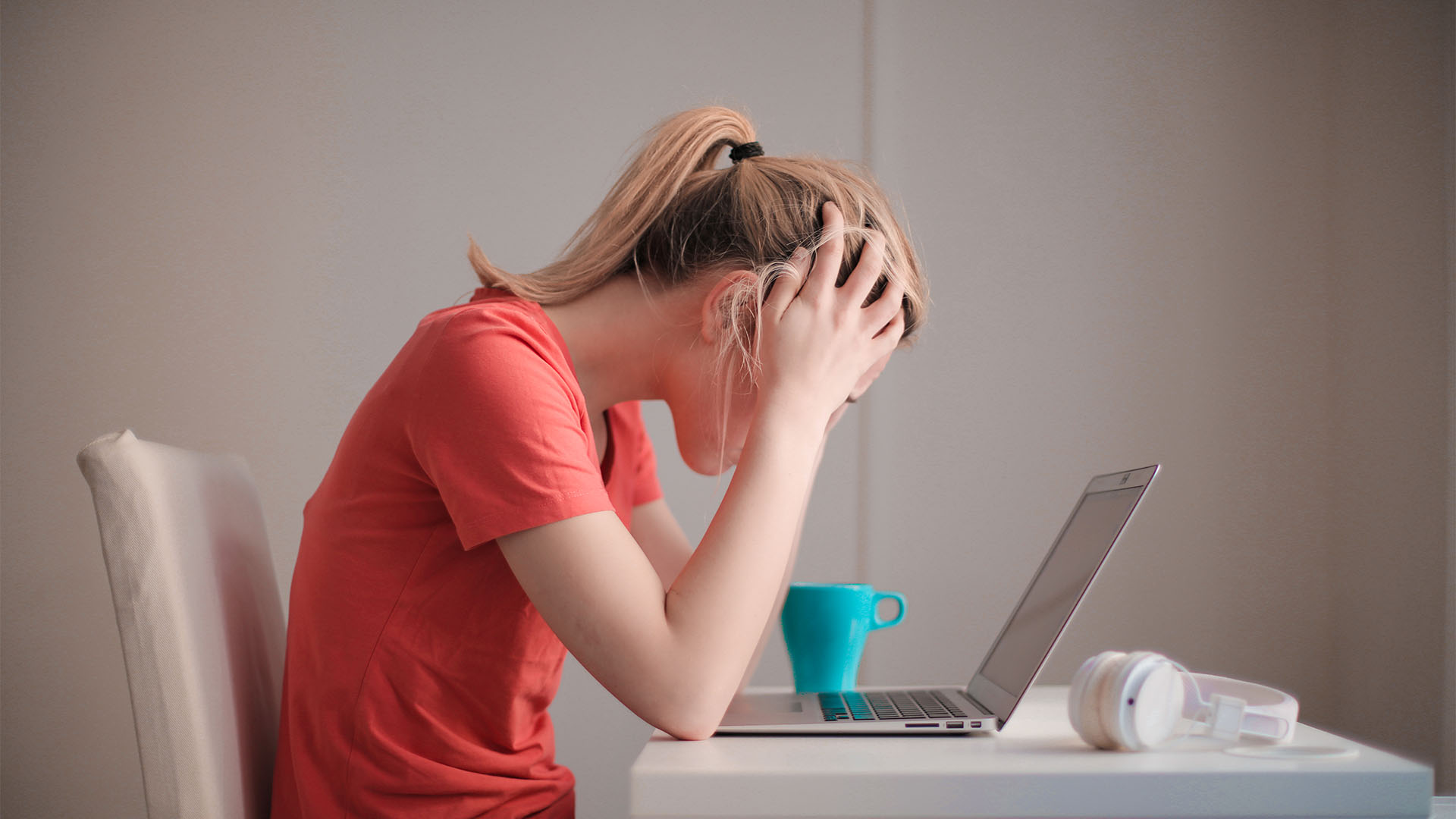 A college student sitting in front of her laptop alone, holding her head with hands.